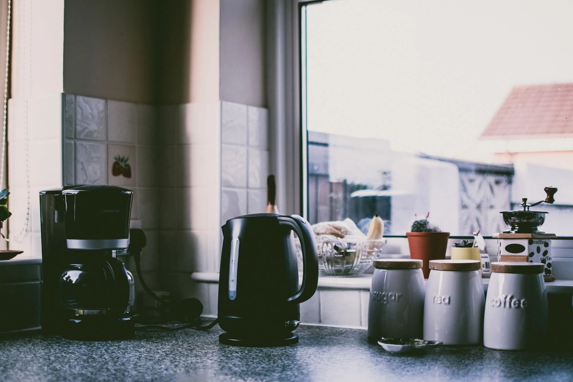 A kettle and storage tins on a kitchen counter beside a window